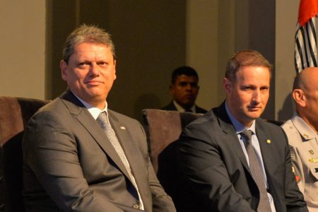 PCC Imagem colorida do governador de São Paulo Tarcísio de Freitas sentado ao lado do secretário de Segurança Pública Guilherme Derrite. Os dois estão vestidos de terno e gravata