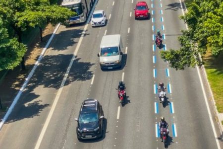 Imagem colorida mostra uma avenida do alto com carros andando em três faixas e, na quarta faixa, pintada na cor azul, andam apenas motos - Metrópoles