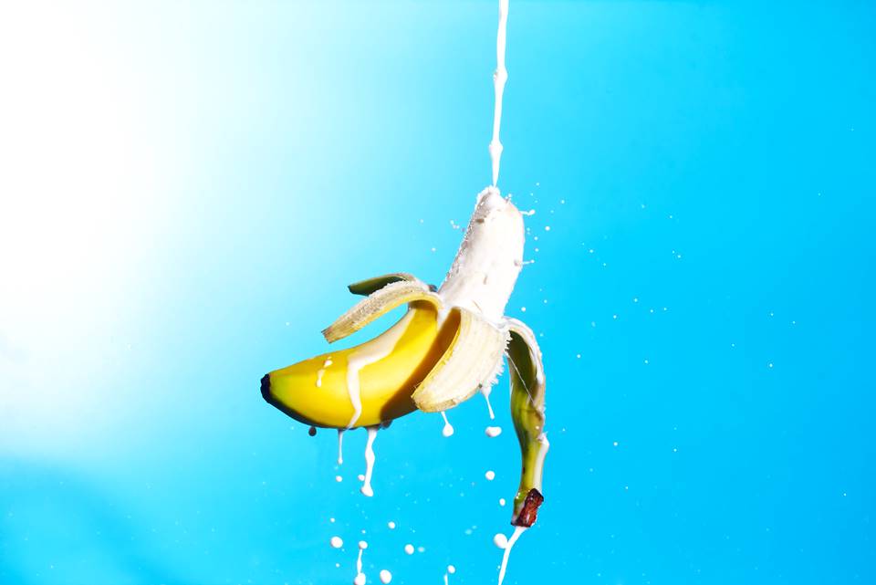 Banana sendo atingida por jato de leite em fundo azul - Metrópoles