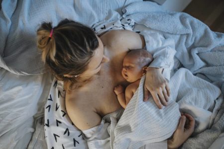 Mãe segurando criança recém nascida em cama de hospital