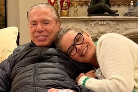 Silvio Santos com Cintia Abravanel abraçada nele de lado, ambos sentados em sofá - metrópoles