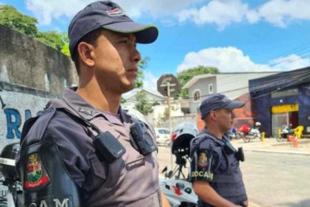 Imagem colorida mostra policiais militares vestidos com uniformes da corporação, camisa e boné cinzas, colete à prova de bala e câmeras corporais na altura do peito - Metrópoles