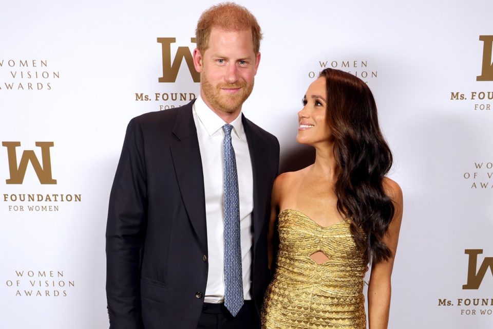 Foto colorida de homem ruivo, branco e vestido com terno ao lado de mulher negra com roupa dourada - Metrópoles