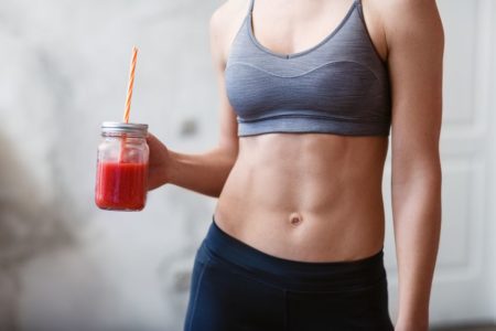 Foto colorida. Imagem foca em uma mulher com barriga bem definida e está tomando um liquido vermelho - Metrópoles