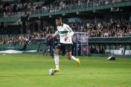 Homem negro, vestido de uniforme branco, corre em gramado de futebol com bola ao lado do pé direito - Metrópoles