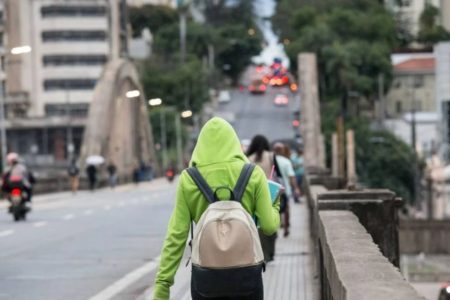 Imagem colorida de uma pessoa usando um agasalho verde caminhando pelas ruas de Belo Horizonte durante onda de frio - Metrópoles