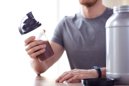 Imagem colorida de homem segurando um recipiente com Whey Protein, suplemento - Metrópoles