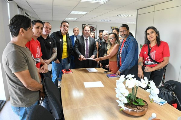 Fotografia colorida de grupo de pessoas em pé rodeando mesa