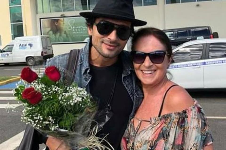 Jeff Machado e a mãe, Maria das Dores. Ele está de óculos de sol, com um chapéu preto, jaqueta escura e camisa preta. Ela está com óculos de sol e roupa colorida - Metrópoles