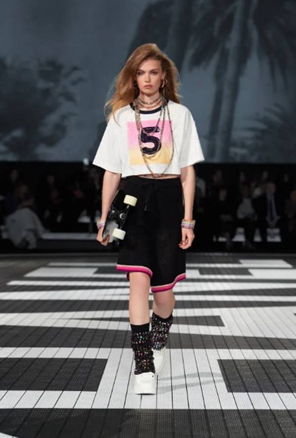 Na passarela da Chanel, modelo usa look com bermuda preta larga e detalhes em rosa com camiseta oversized branc - Metrópoles