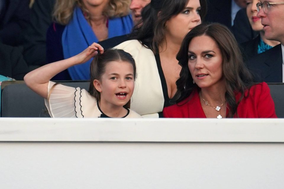 Foto colorida de menina branca, loira e com a mão no cabelo ao lado de mulher branca, com cabelo castanho e roupa vermelha - Metrópoles