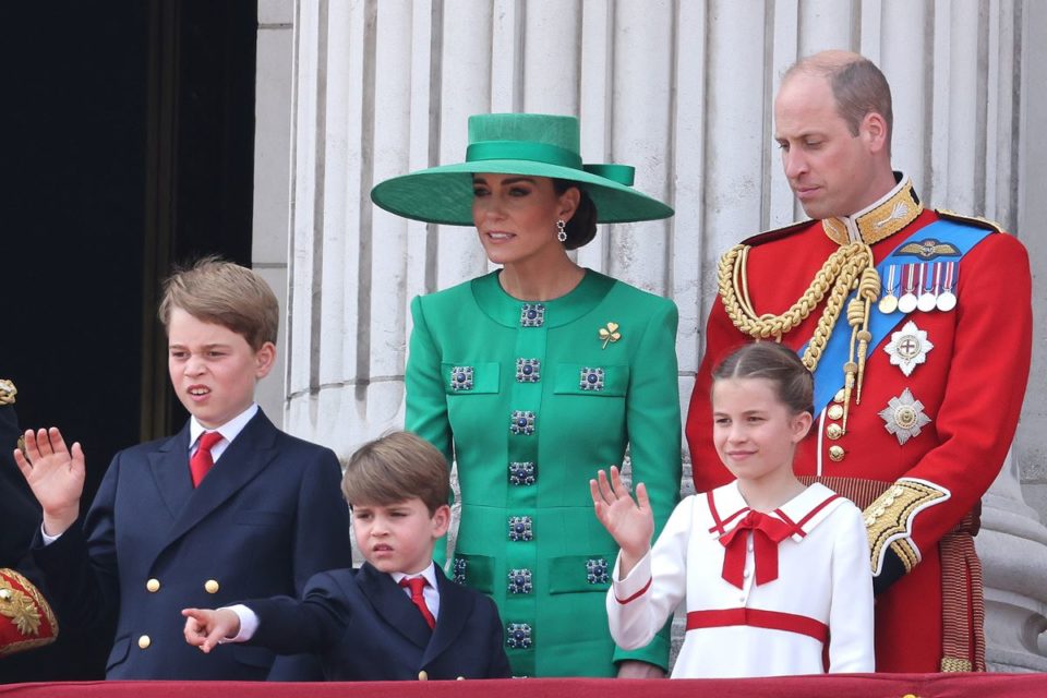 Foto de mulher com roupa verde ao lado de homem calvo e com traje militar do Reino Unido. À frente dos adultos, há três crianças, sendo dois meninos e uma menina - Metrópoles