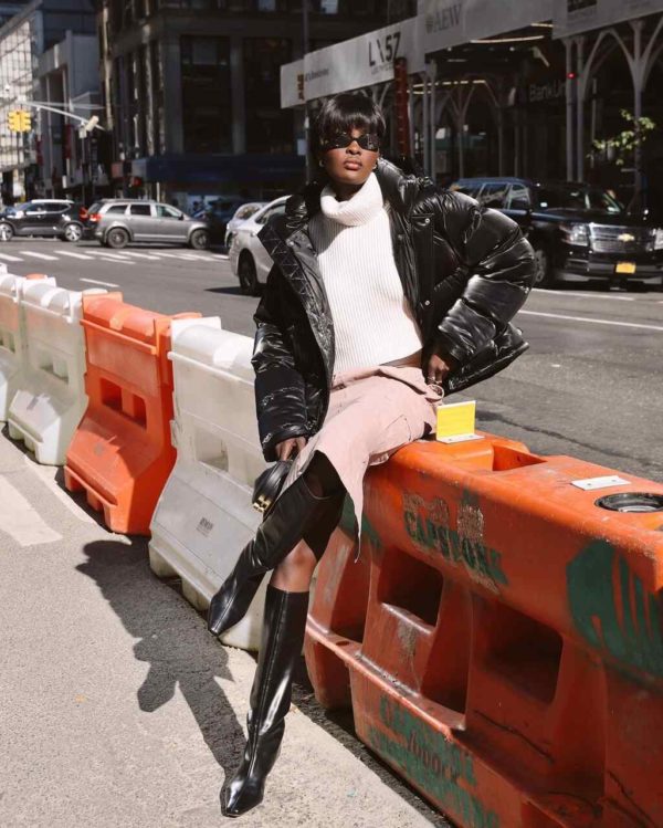 Na imagem com cor, uma mulher negra usando um tricot branco e uma saia bege cor com botas pretas - Metrópoles