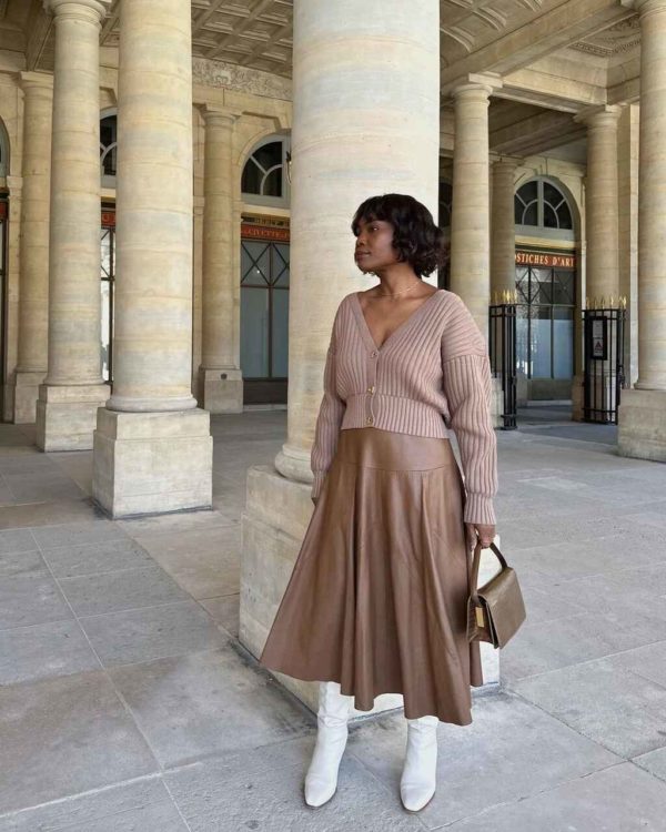 Na imagem com cor, uma mulher negra usando um tricot marrom e uma saia da mesma cor com botas brancas - Metrópoles