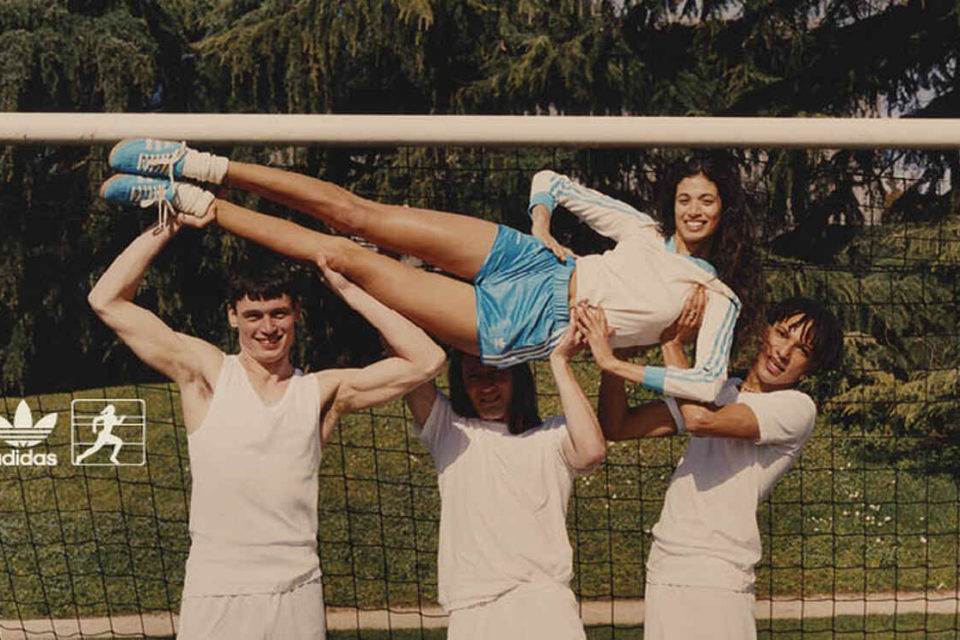 Na imagem com cor, 3 homens segurando uma mulher na frente de um gol - Metrópoles