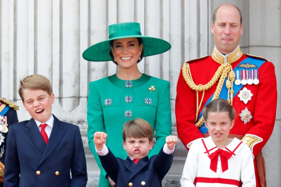 Foto colorida de mulher branca e com roupas verdes ao lado de homem calvo e branco com trajes militares. À frente do casal, há três crianças loiras, sendo dois meninos com blazer e gravata. Também há uma menina com roupa branca com laço vermelho - Metrópoles