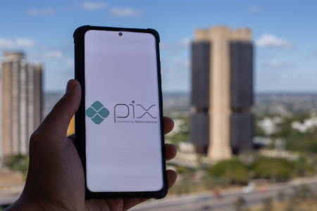 Mão segura celular, com tela branca escrita Pix, em frente à sede do Banco Central - Metrópoles