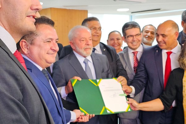 Fotografia colorida de presidente segurando documento com pessoas ao redor