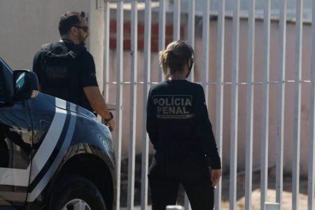 Fotografia colorida mostra dois policiais penais de costa com uniforme