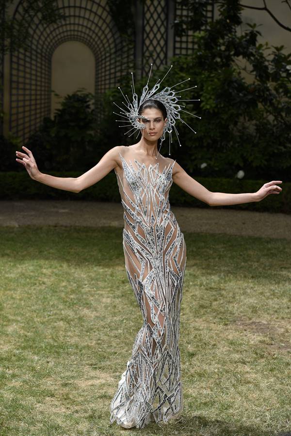 Em fundo de grama, modelo usa vestido longo com brilho e enfeite na cabeça - Metrópoles