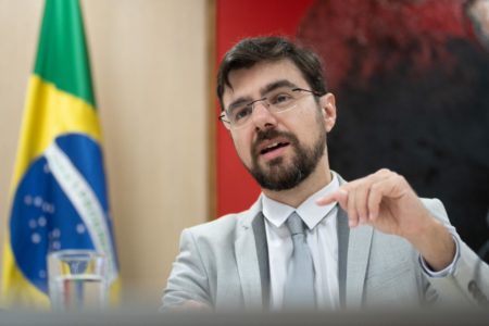 Foto colorida do secretário Guilherme Mello, à frente de bandeira do Brasil - Metrópoles