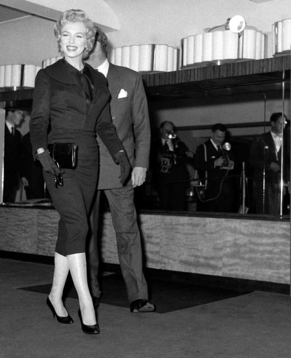 Na imagem preto e branco, uma mulher branca em pé vestida toda de preto e salto - Metrópoles