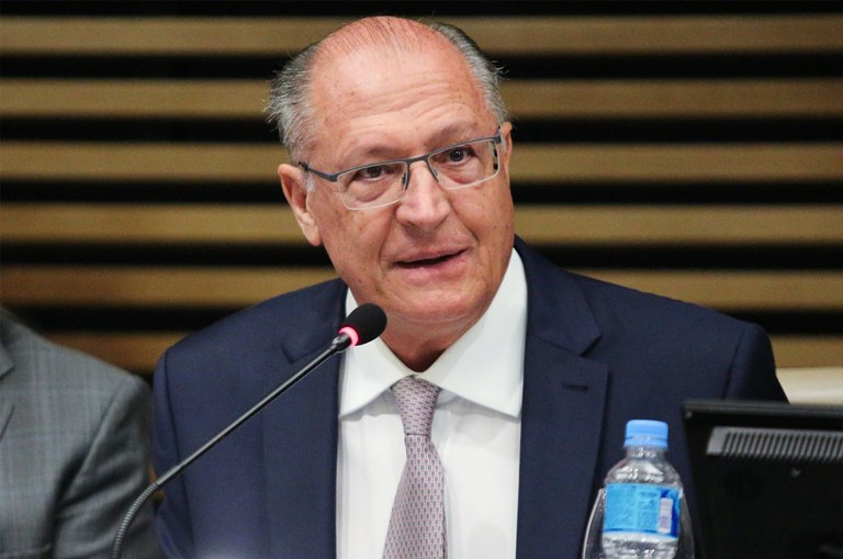 Geraldo Alckmin sentado, de óculos e terno, fala ao microfone - Metrópoles