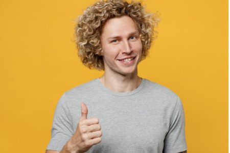 Na imagem, homem branco de cabelo loiro usando uma camiseta cinza em um fundo amarelo - Metrópoles