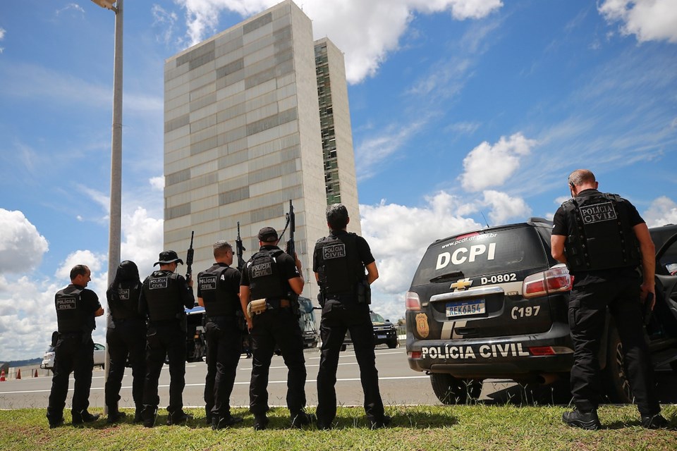 Agentes da PCDF parados em frente ao Congresso Nacional. Estão de costas, vestem uniforme e seguram fuzis