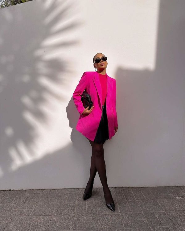 Na imagem com cor, uma mulher negra usando um blazer e blusa rosa com saia e meia-calça preta - Metrópoles