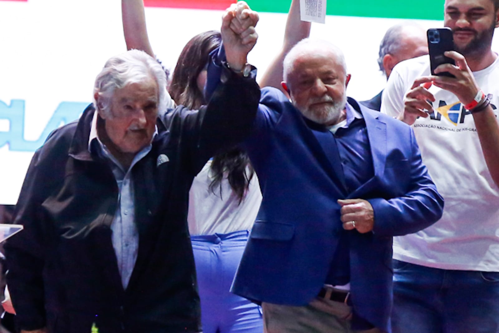 Imagem colorida mostra ex-presidente do Uruguai Pepe Mujica de mão dada com o presidente Luiz Inácio Lula da Silva no palco do congresso da UNE