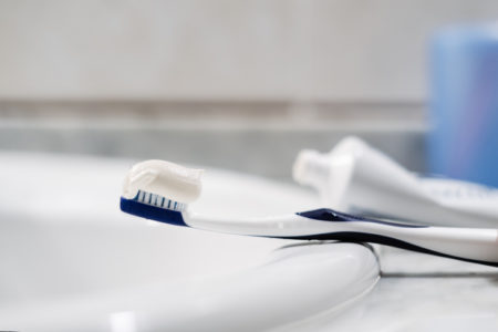 Foto em close-up mostra uma escova de dentes numa pia de banheiro com pasta de dente sobre ela - Metrópoles