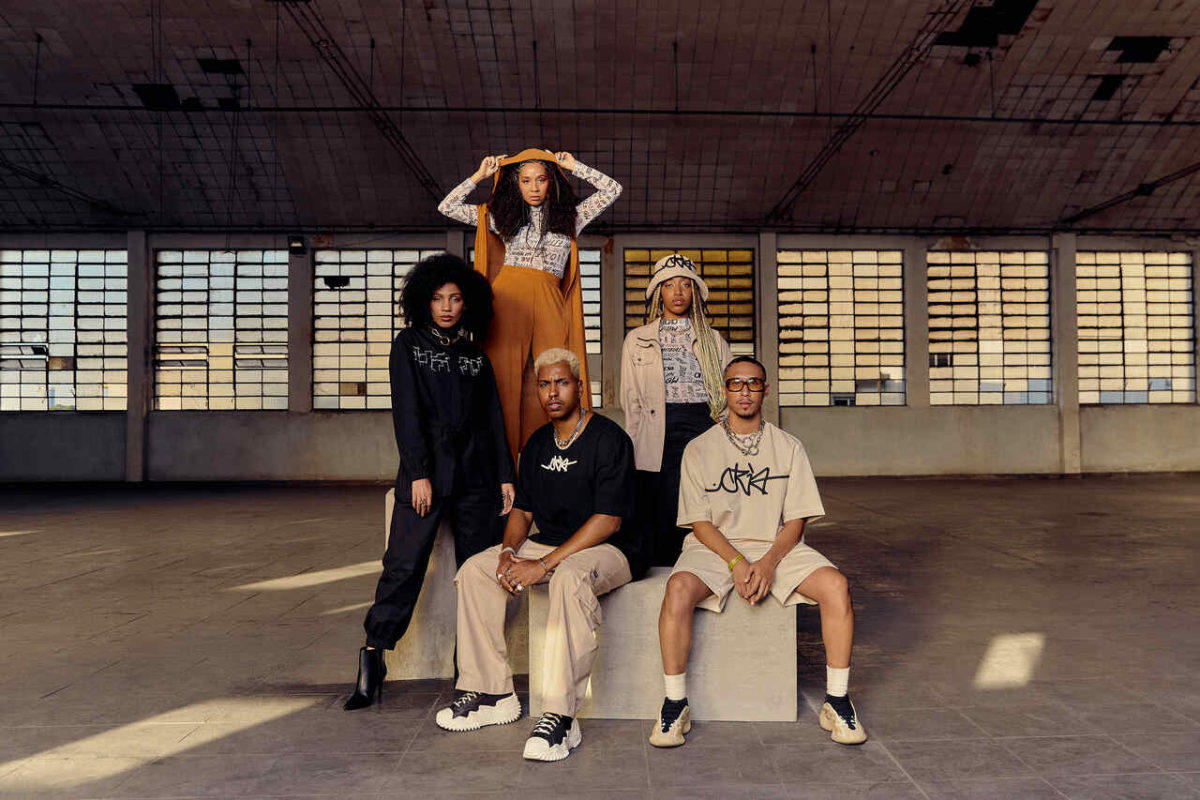 Na imagem com cor, 5 pessoas em um banco branco posando para uma foto editorial da Riachuelo - Metrópoles