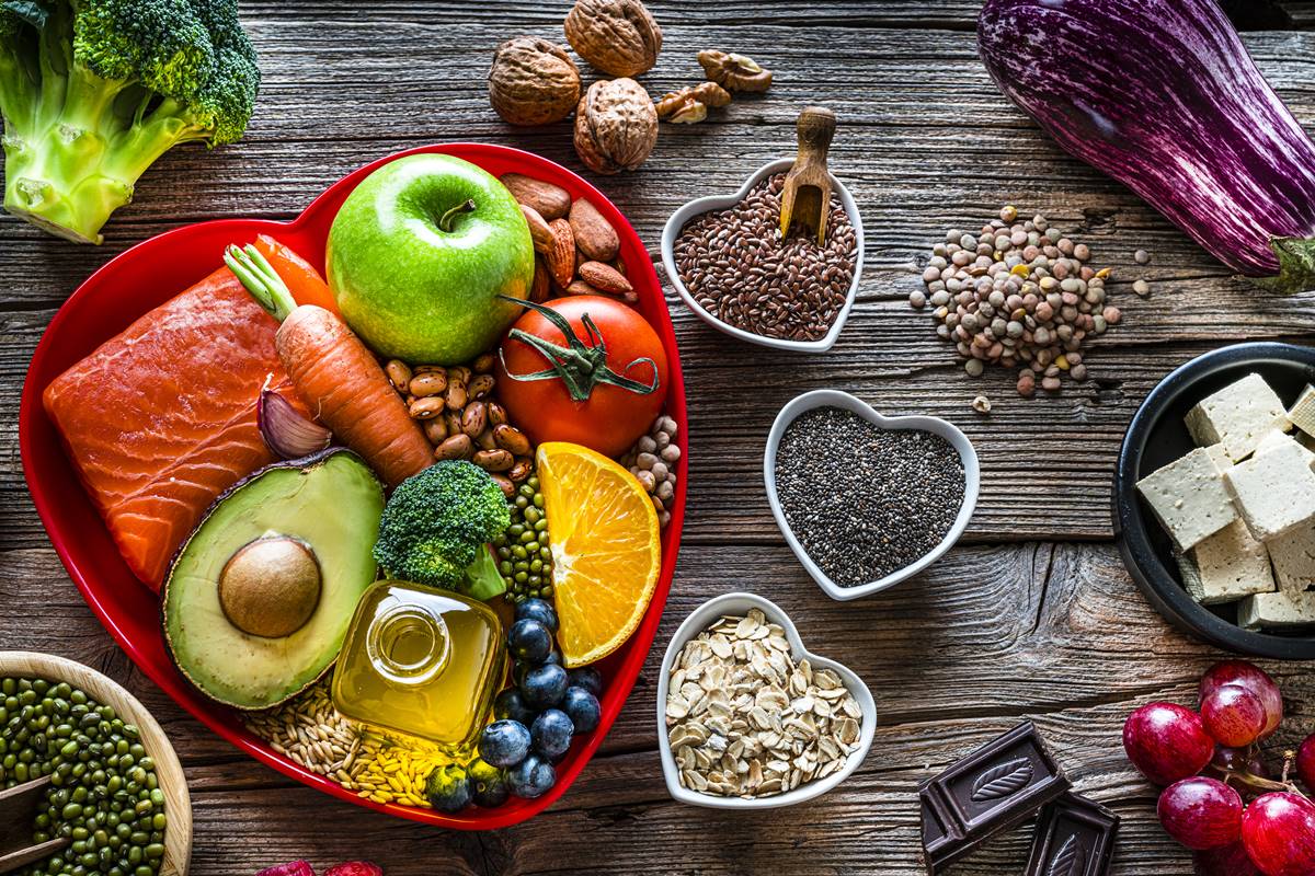 Foto colorida de prato em formato de coração com frutas, peixe, verduras dentro. Do lado, há potes pequenos, em formato de coração, com grãos e oleaginosas dentro - Metrópoles