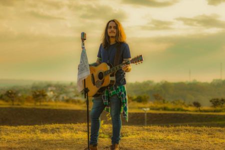 Foto colorida do cantor Cezar Degraf segurando um violão - Metrópoles