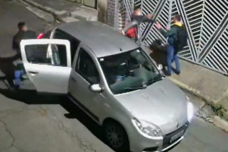 Veículo prata com portas traseiras abertas; um homem aponta arma para outro ao lado do carro - Metrópoles