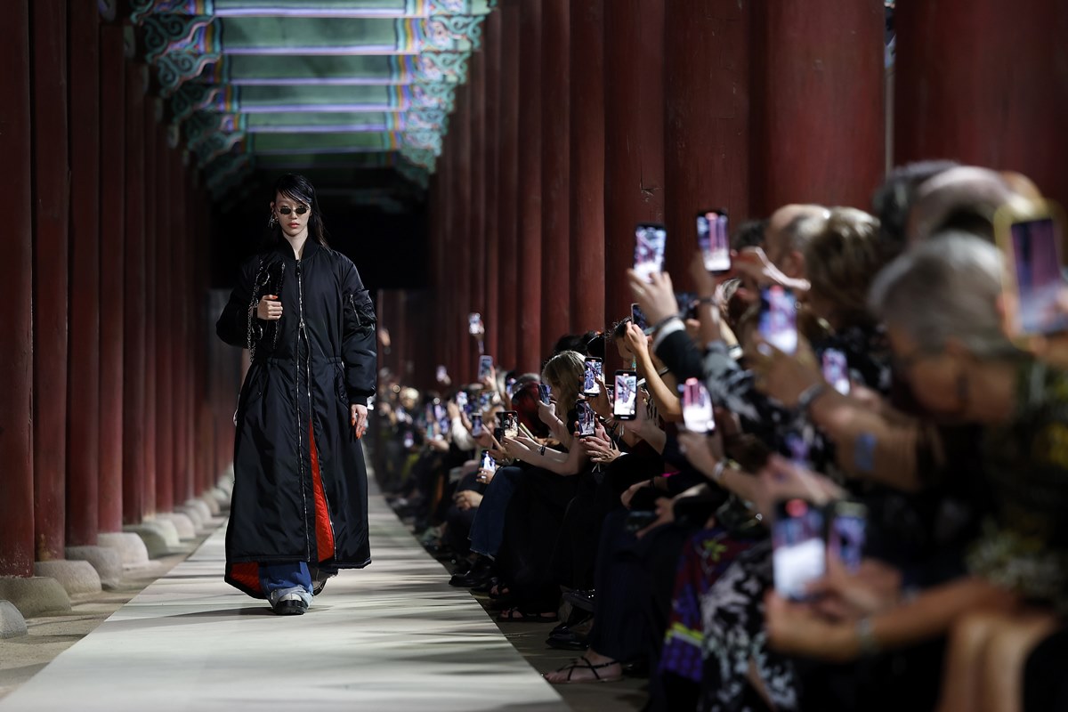 Na imagem com cor, modelo desfila com vestido preto enquanto a plateia a filma - Metrópoles