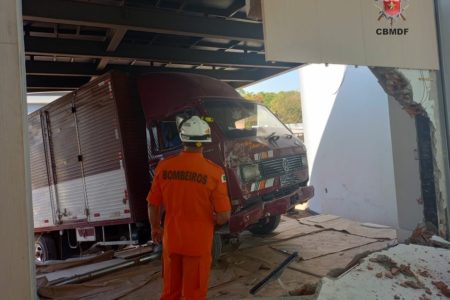 Caminhão vermelho e branco parado sob telhado, em casa com parede destruída de entrada