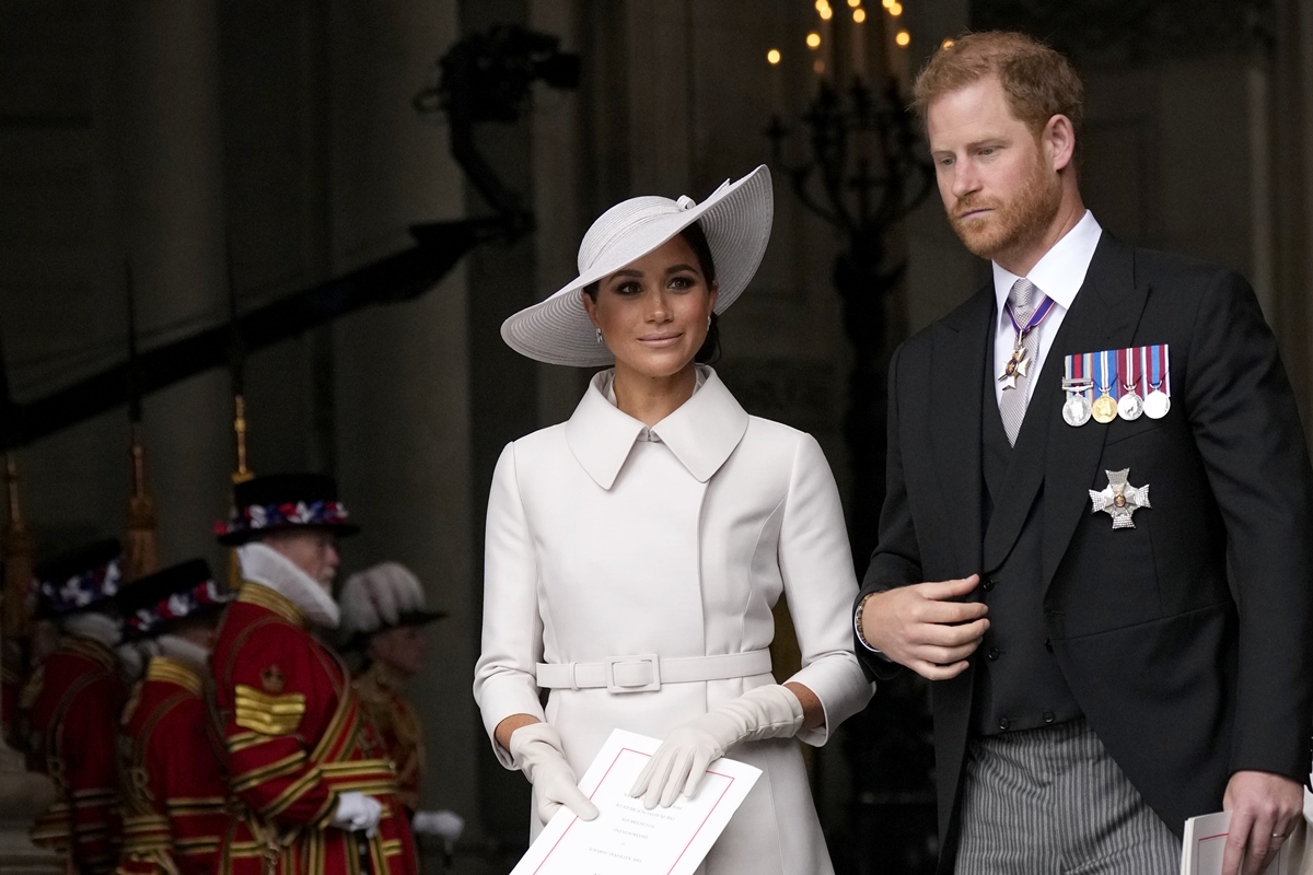 Foto colorida. Mulher negra usa um vestido e um chapéu branco. Ao seu lado, está um homem branco, de cabelos ruivos. Ele está vestindo um terno preto com algumas medalhas de honra e uma camisa branca