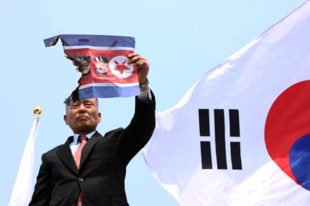 Foto colorida de manifestante sul-coreano rasgando a bandeira da Coreia do Norte - Metrópoles