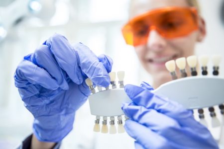 Imagem colorida mostra mulher dentista de óculos laranja escolhendo a tonalidade de lente de contato dentária - Metrópoles