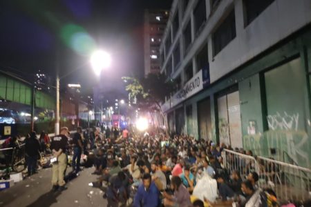 Fotografia à noite mostra grande número de pessoas sentadas na rua durante operação policial na cracolândia - metrópoles