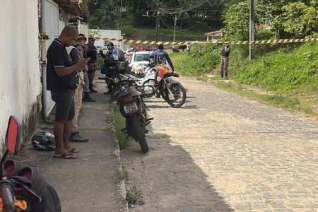 Foto colorida de rua interditada, homem com celular na mão e moto encostada em muro - Metrópoles