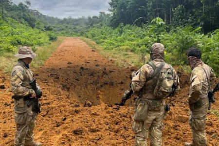 Foto colorida de militares armados de costas, olhando para pista de pouso clandestina destruída - Metrópoles