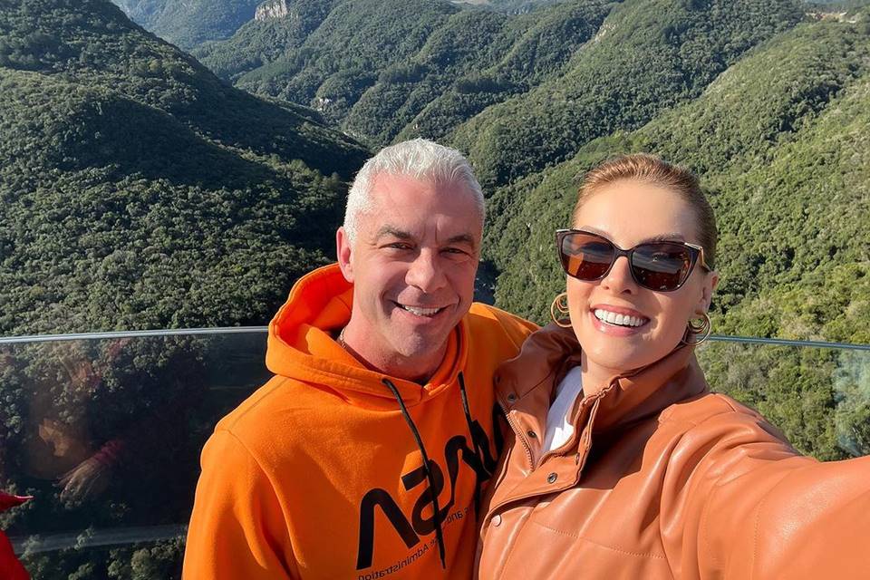 Foto colorida de Ana Hickmann e Alexandre Correa. Ela está de óculos de sol, com uma roupa laranja. Ele está de casaco laranja - Metrópoles