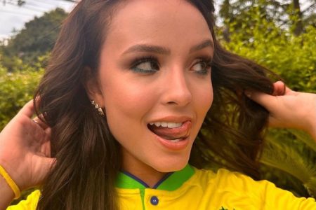 Larissa Manoela está com uma camisa do Brasil e olhando para o lado. Ela é branca e tem o cablo escuro - Metrópoles