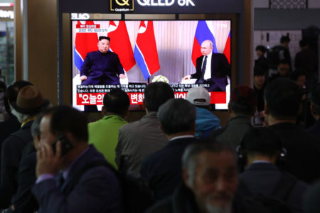 Foto colorida de pessoas assistindo pela televisão o encontro entre Kim Jong-un e Putin - Metrópoles