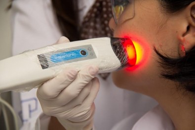 Foto mostra faixo de luz vermelha sendo aplicada por pessoa de jaleco no rosto de uma mulher
