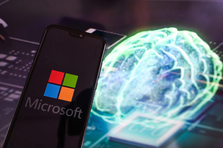 Imagem colorida de telefone celular com o logotipo da Microsoft. Ao fundo, a imagem de um cérebro - Metrópoles