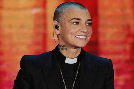 foto colorida de Sinéad O'Connor com batina e fundo laranja - Metrópoles